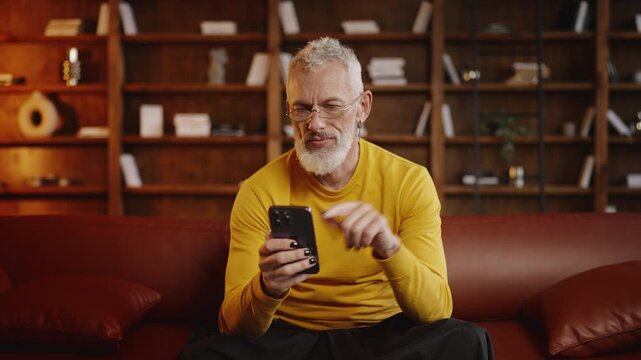 Stylish middle-aged man scrolling through social media on a phone at home