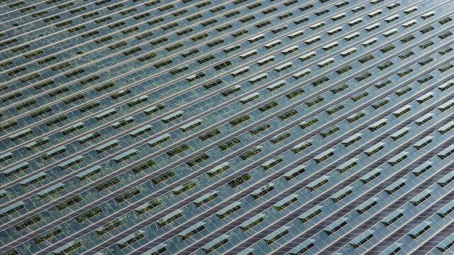 Aerial view of an agrivoltaic greenhouse with integrated photovoltaic panels on a glass roof, featuring repeating diagonal patterns in Saulce-sur-Rhone, Auvergne-Rhone-Alpes, France.
