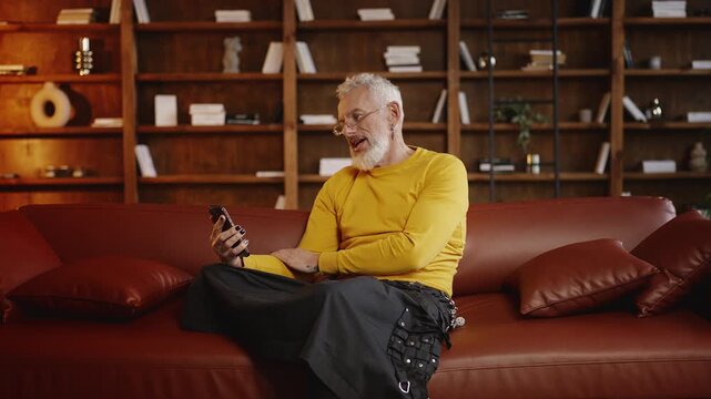 Silver-haired man in stylish outfit having an online video call on a phone