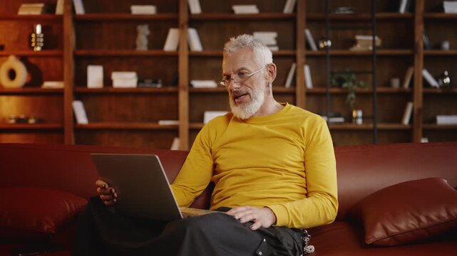 Fashionable man in his 50s talking with a colleague during a laptop video call
