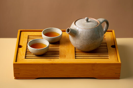 Traditional ceramic teapot and cups on wooden chaban tea tray. Beige and brown background. Close up.