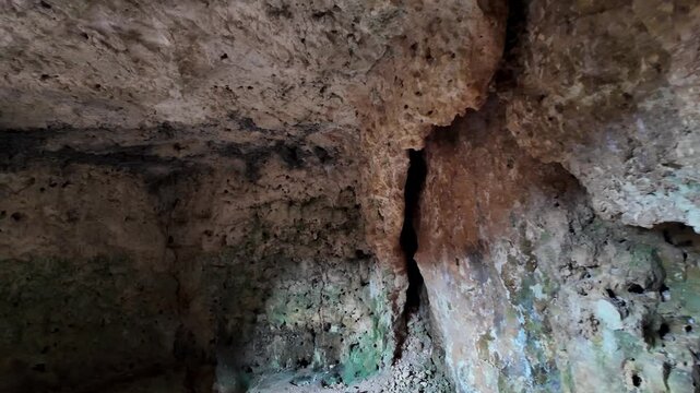 Xemxija, Malta 29.07.2026 - Heritage trail, Roman Baths, shelf like cut in the stone Dark cave walls show rough, textured surfaces. Greenish moss grows on damp, uneven stone. Light filters through nar