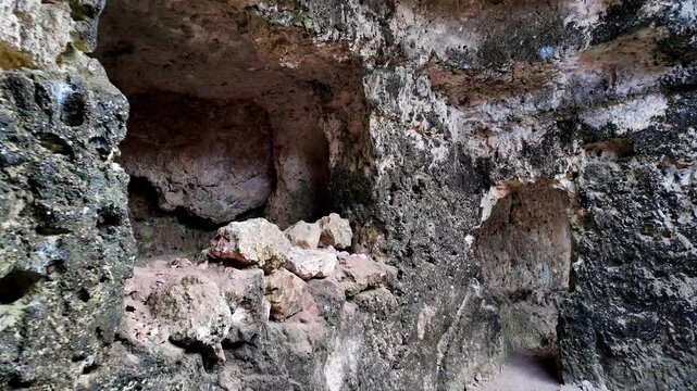 Xemxija, Malta 29.07.2026 - Heritage trail, Roman Baths, shelf like cut in the stone Dark cave walls show rough, textured surfaces. Greenish moss grows on damp, uneven stone. Light filters through nar