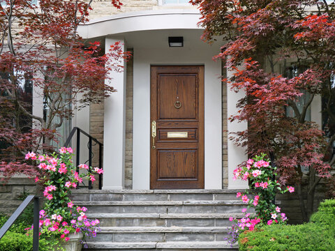 Elegant wood grain front door with Japanese maple and pink mandevilla flowers