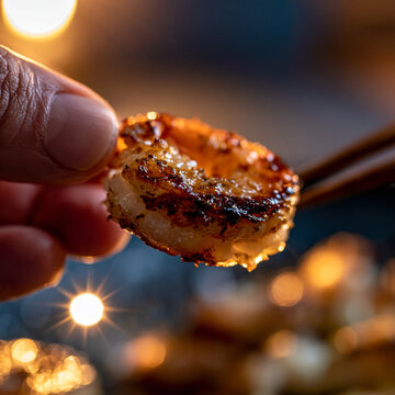 Hand holding perfectly seared shrimp piece using chopsticks with chopsticks shellfish appetizer
