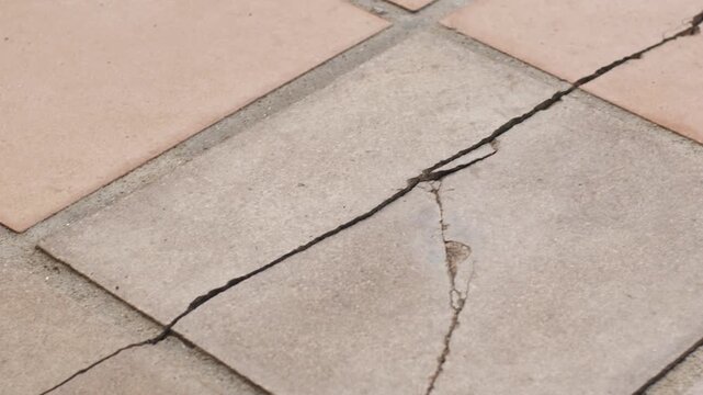 Damaged ceramic floor tile with a long crack. Concept of home maintenance, ground subsidence, construction defect, and house repair.