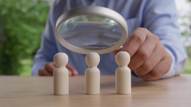 Human resources recruitment concept with magnifying glass inspecting wooden figures one by one, candidate screening, employee selection, talent acquisition, background verification and hiring process