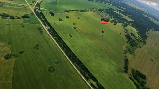 A parachutist performs a flight under a sports dome over rural fields. Aerial view of the summer landscape and extreme sports.
