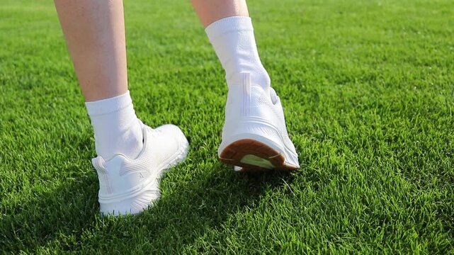 Young woman checks a blister bandage on her heel after walking or sports activity on a green stadium field. Close-up of foot discomfort caused by uncomfortable shoes, highlighting foot care, injury