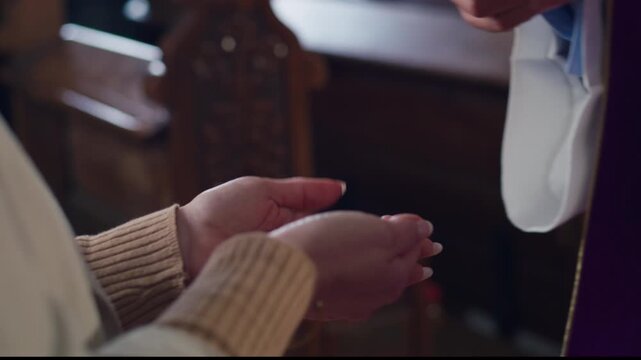 Priest placing the Host in the palm of the woman receiving Communion, and she putting the Eucharistic bread into her mouth.