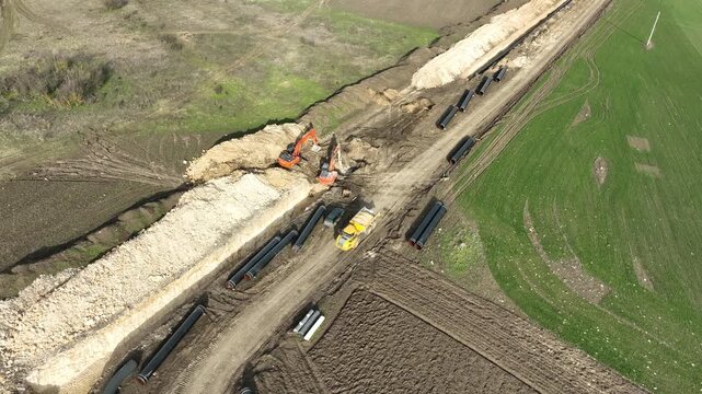 Aerial view of a major pipeline construction project. Heavy machinery including excavators and pipelayers install a new gas line in a rural field. Industrial energy infrastructure development.