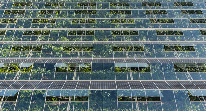 Aerial view of a modern agrivoltaic greenhouse with solar panels integrated into a glass roof, showing a geometric grid pattern over green crops in Saulce-sur-Rhone, Auvergne-Rhone-Alpes, France.