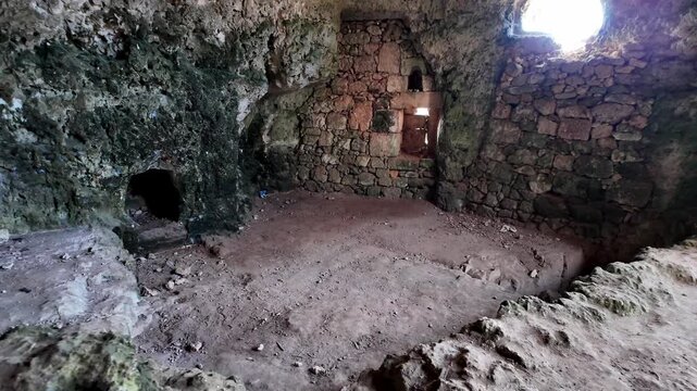 Xemxija, Malta 29.07.2026 - Heritage trail, Roman Baths, shelf like cut in the stone Dark cave walls show rough, textured surfaces. Greenish moss grows on damp, uneven stone. Light filters through nar