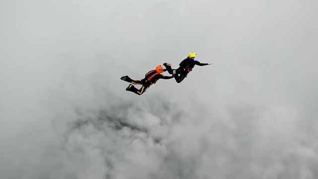 Two athletes perform aerial acrobatics in free fall among the clouds. Extreme sports, adrenaline and speed at high altitude.
