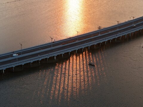 Aerial view of the Mandara Toll Road bridge over the water at sunset with long shadows cast on the surface in Kabupaten Badung, Bali, Indonesia.