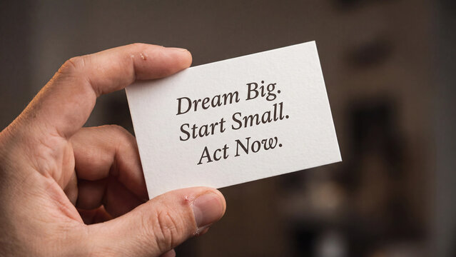 Hand holding a white business card with motivational text dream big start small act now
