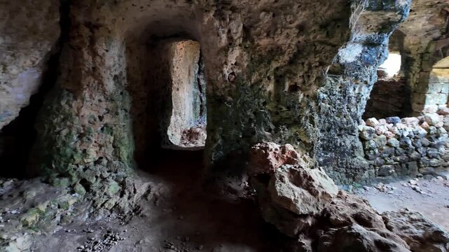 Xemxija, Malta 29.07.2026 - Heritage trail, Roman Baths, shelf like cut in the stone Dark cave walls show rough, textured surfaces. Greenish moss grows on damp, uneven stone. Light filters through nar