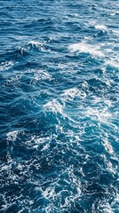 Fototapeta premium A high angle view of deep blue ocean water with white foam waves created by a moving boat on a sunny day