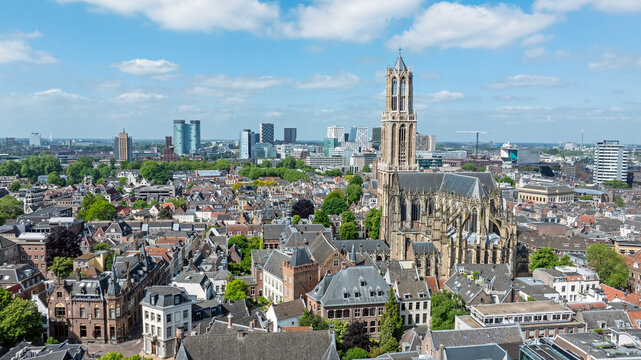 Aerial view of Dom Tower rising above the historic city center with dense rooftops, urban architecture, and a bright blue sky in Utrecht, Utrecht, Netherlands.