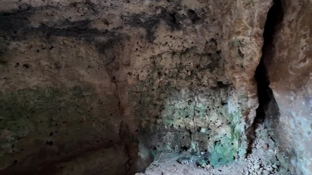 Xemxija, Malta 29.07.2026 - Heritage trail, Roman Baths, shelf like cut in the stone Dark cave walls show rough, textured surfaces. Greenish moss grows on damp, uneven stone. Light filters through nar