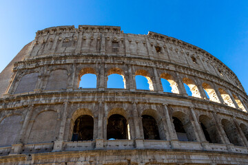 Obraz premium Famous Coliseum in Rome. Colosseum, or Coliseum. Part of the wall of an antique stone structure with arches. Italy, Europe. Famous touristic place in the world, Europe. Beautiful blue sky background.