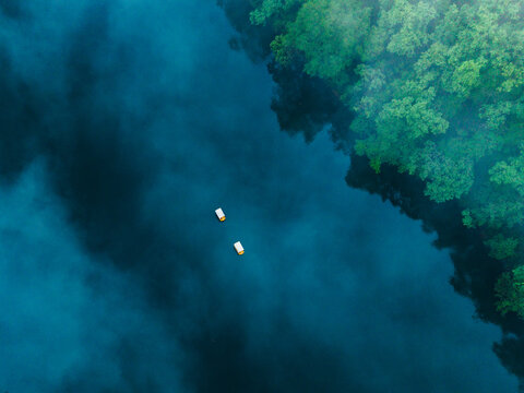 Aerial view of two small boats floating on a dark blue lake surrounded by dense green forest in the misty mountains of Uttarakhand, India.