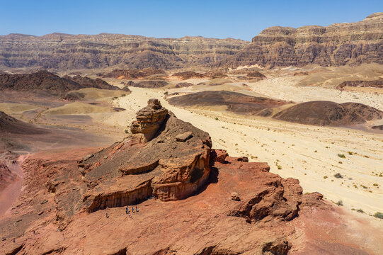 Aerial view of the red sandstone rock formations at Timna Park with visitors walking on the rugged desert terrain in Eilat, South District, Israel.