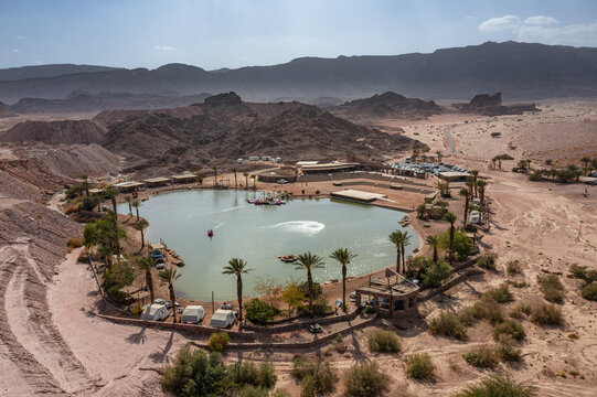 Aerial view of Timna Park lake surrounded by desert mountains, palm trees, and small structures in Eilat, South District, Israel.
