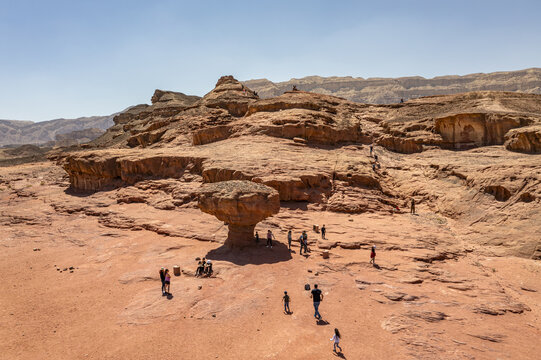 Aerial view of the Mushroom rock formation in Timna Park, surrounded by rugged desert landscape, sandstone cliffs, and visitors walking on the sandy ground in Eilat, South District, Israel.