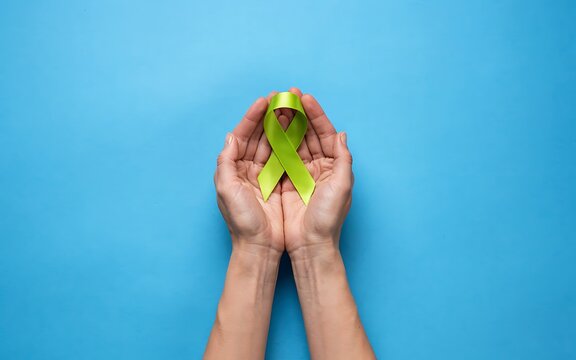 Hands holding a green awareness ribbon isolated on a blue background for medical support concepts