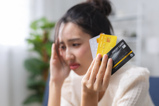 Stressed woman holding credit card at home, representing debt, financial hardship, credit payment, personal finance, budgeting, money problems, economic pressure, financial stress.