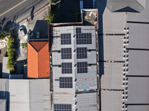 Aerial view of Bali Swim swimwear manufacturer facility featuring solar panels installed on a metal roof with an adjacent orange tiled section in Kecamatan Denpasar Barat, Bali, Indonesia.