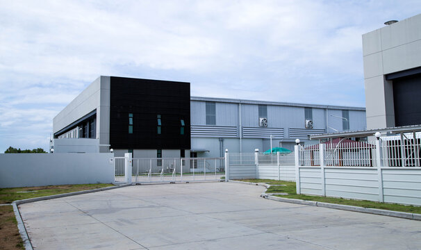 Modern factory building exterior with office area and parking lot in industrial estate,Exterior view of modern warehouse and industrial plant building with blue sky