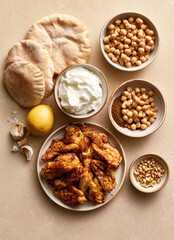 Fototapeta premium Ingredients for Mediterranean chicken shawarma bowl with pita bread, chickpeas, yogurt sauce, pine nuts, and lemon, top view.