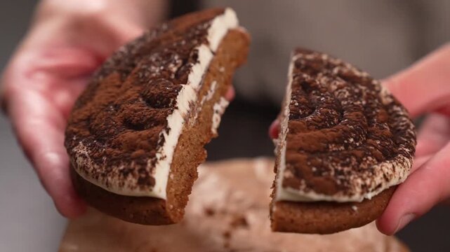 Close-up of a pastry chef's hands showing a tiramisu cookie cut in half.