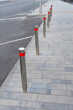 Stainless steel bollards with reflective red bands line a paved sidewalk beside accessible parking spaces, improving pedestrian safety and urban traffic management.