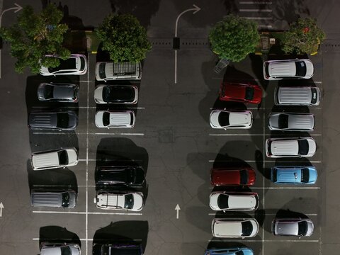 Aerial view of the Lotte Mart parking lot at night with rows of parked cars on asphalt in Kecamatan Denpasar Selatan, Bali, Indonesia.
