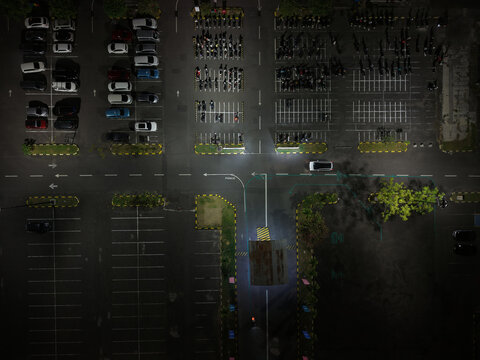Aerial view of Parkir Lotte Mart at night with rows of parked cars and motorcycles illuminated by artificial lighting in Kecamatan Denpasar Selatan, Bali, Indonesia.