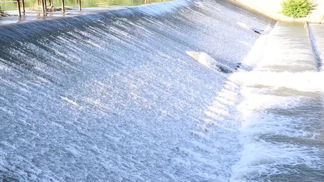 Badam River flows at high speed through floodgate sluices after heavy rain, creating powerful water discharge and cascading rapids.