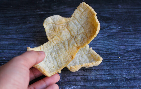 Hands holding two rambak snacks on a black board.