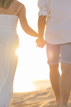 Young couple holding hands on the beach during sunset while walking along the shore