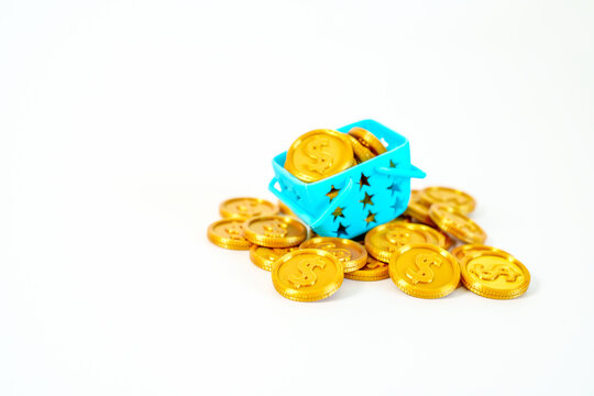A blue miniature shopping basket overflowing with gold dollar coins on a white background. Concept for consumerism, wealth, commerce, and grocery spending. High-quality studio shot.