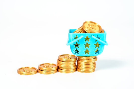 Rising stacks of gold coins form a growth chart with a blue shopping basket full of money on top. Concept of retail success, wealth accumulation, and investment growth on a white background.