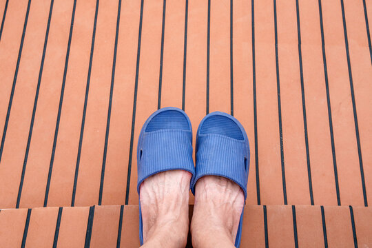Top down view of feet wearing blue rubber sandals on a teak deck with black lines. Relaxing vacation vibe on a boat or luxury yacht. Concept of leisure, summer travel, and outdoor relaxation.
