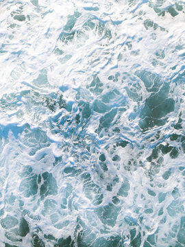 Aerial view of ocean waves crashing against the shore with white sea foam patterns on the water surface in Dee Why, New South Wales, Australia.