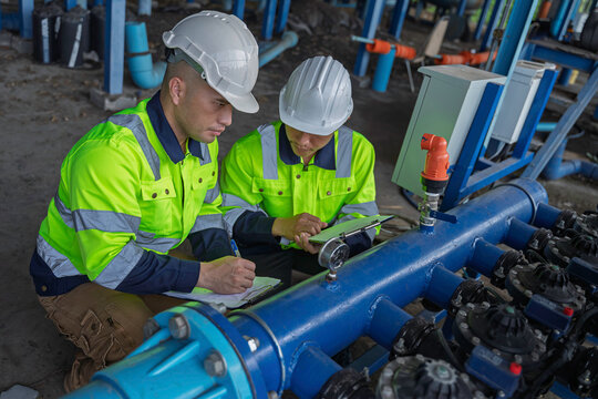 Technicians and engineers inspect a pressure gauge and industrial water pipeline system. Concept of engineering, water management, technical inspection, utilities, and industrial operations.