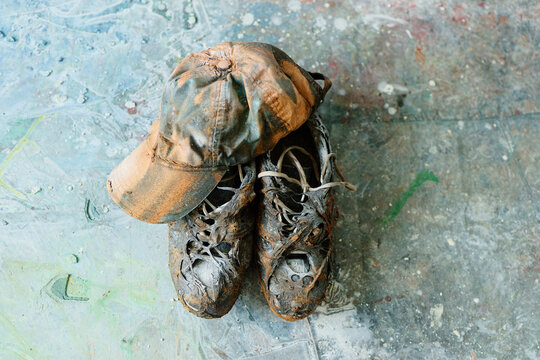 Close up of paint covered cap and worn shoes resting on studio floor, representing contemporary artist process and creative labor. Ideal for art workshop, maker culture, creative industry marketing