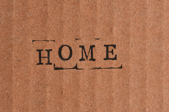 Word HOME centered on textured brown cardboard background, expressing warmth, safety and family.
