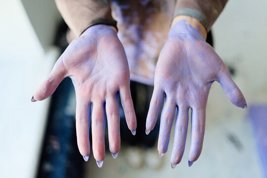 Close up of young adult woman showing paint stained hands while creating contemporary artwork, expressing artistic process and creativity. Useful for art education, studio branding