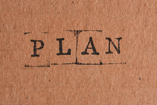 Word PLAN stamped in black ink in center brown paper texture for strategic management.